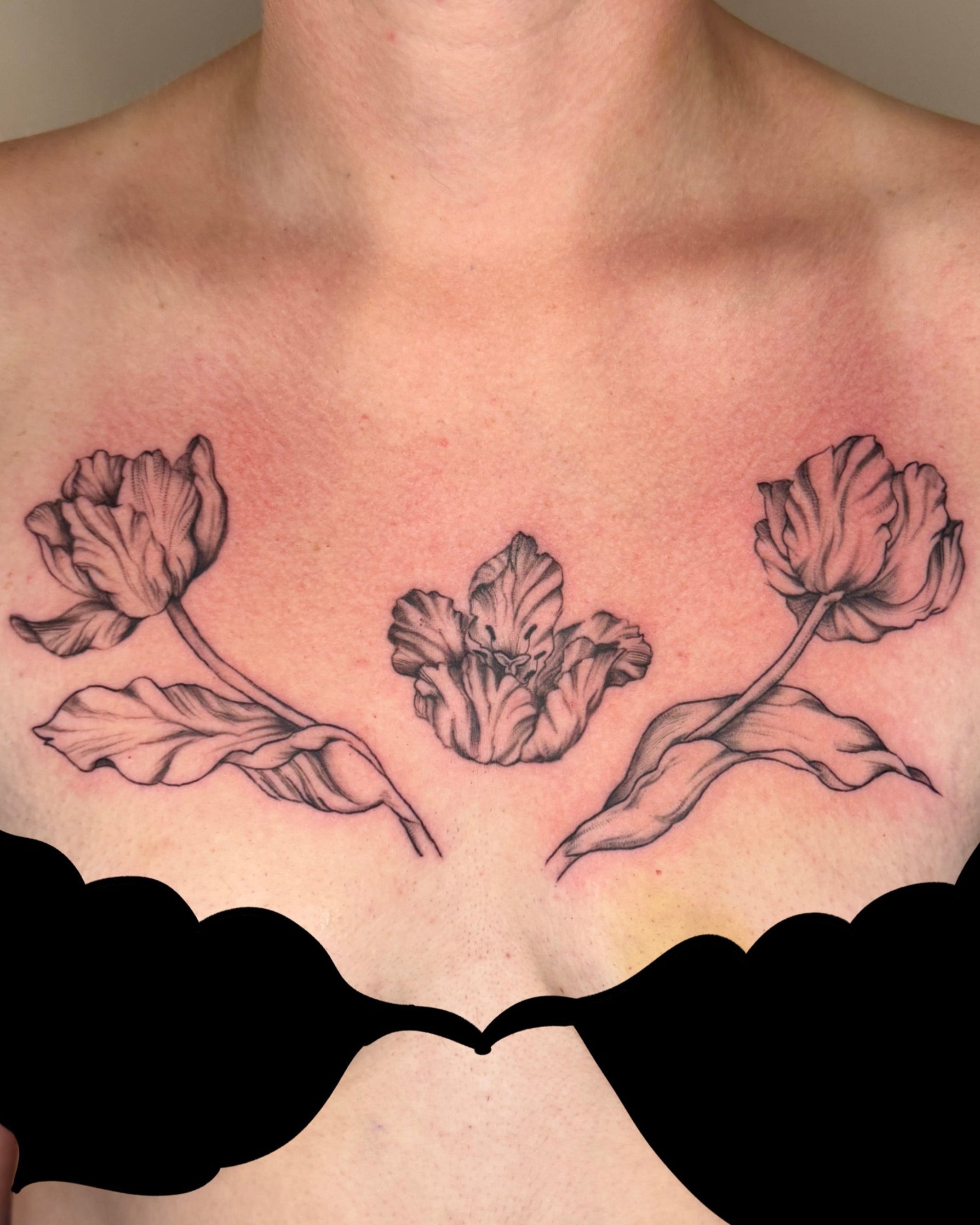 Tattoo of three tulips on a person's chest with a plain background.